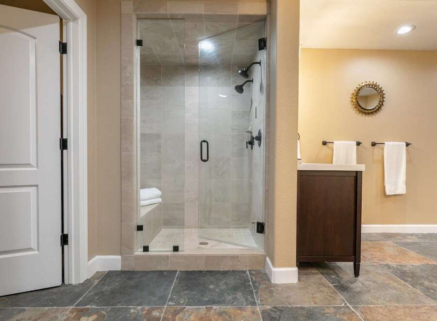 Step into this luxurious bathroom featuring a spacious glass-enclosed shower with multiple showerheads and a built-in bench.