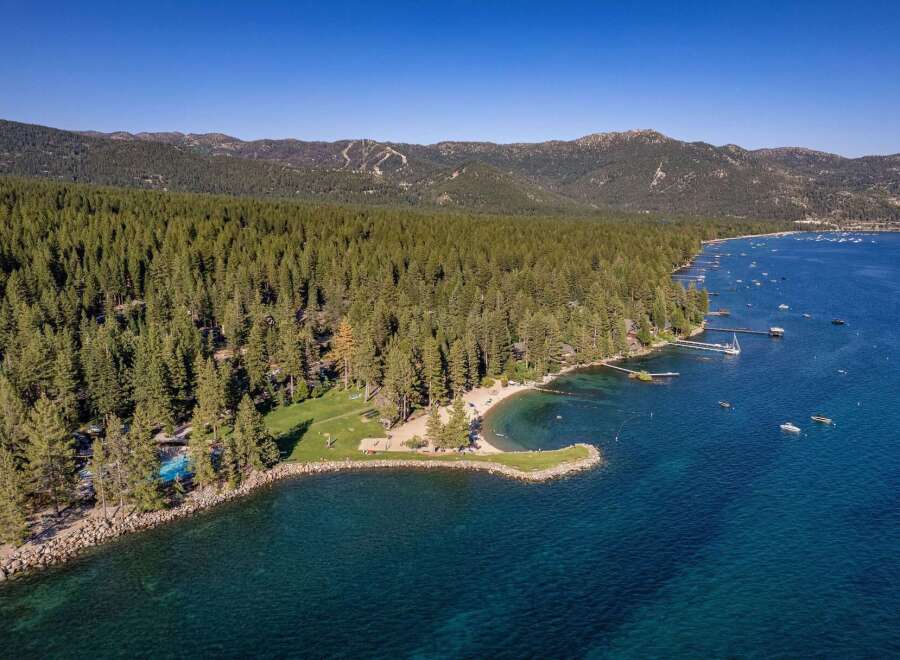 Experience luxury lakeside living with this stunning aerial view of a private beach and pool area nestled within a dense pine forest.