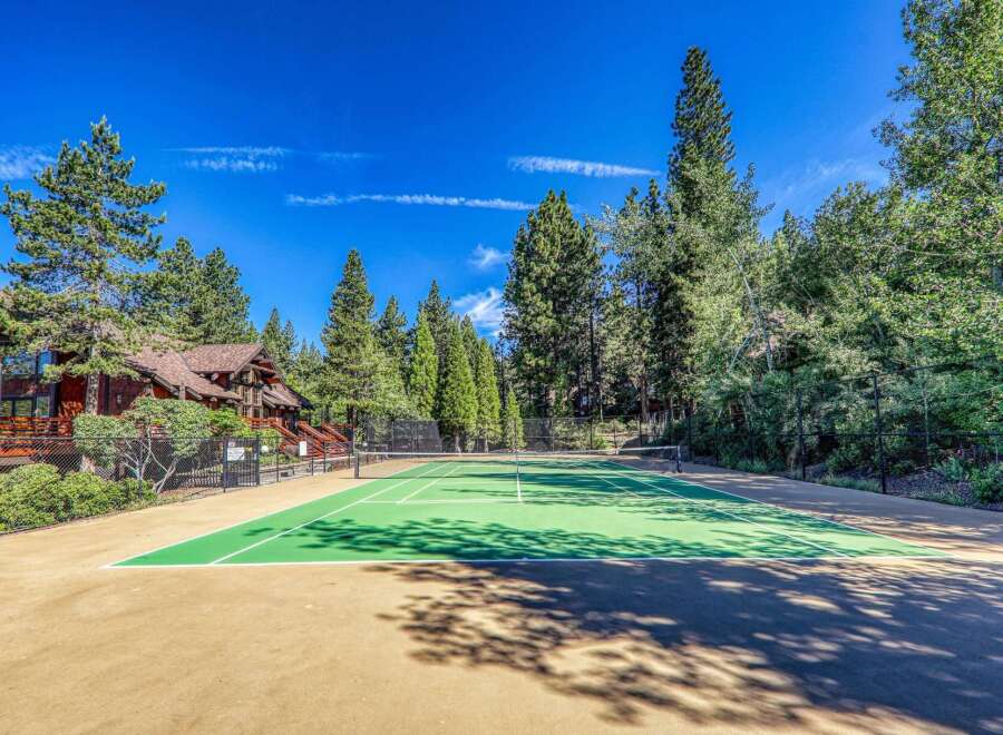 Enjoy outdoor recreation at this stunning property featuring a pristine tennis court surrounded by lush greenery and towering pine trees.