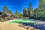 Enjoy outdoor recreation at this stunning property featuring a pristine tennis court surrounded by lush greenery and towering pine trees.