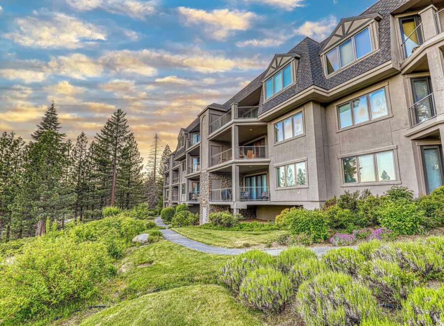 Experience luxury living in this stunning multi-story condo complex nestled amidst lush greenery and towering pine trees.