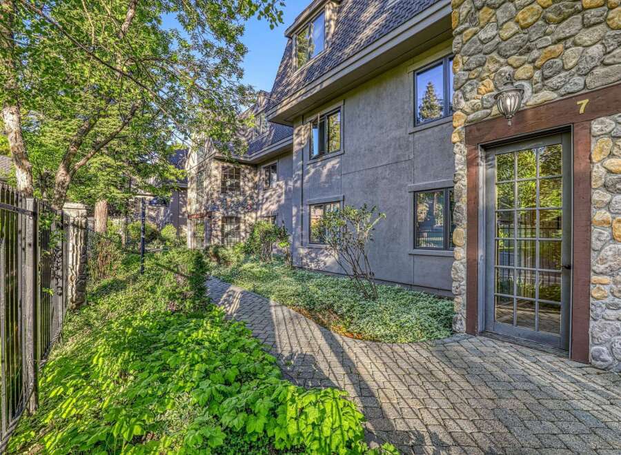 Discover charming architecture with a mix of stone and stucco finishes, complemented by lush greenery and a paved walkway leading to the entrance.