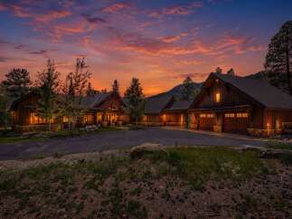 Experience luxurious mountain living in this stunning log home, nestled amidst towering pines and dramatic sunset skies.