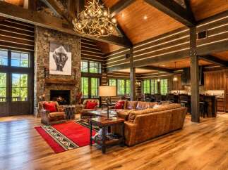 Experience rustic luxury in this stunning log cabin living room, featuring a grand stone fireplace and a magnificent antler chandelier.