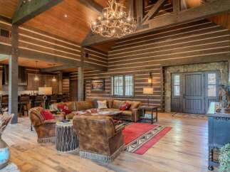 Experience rustic luxury in this stunning log home living area, featuring a grand antler chandelier and a spacious leather sectional.