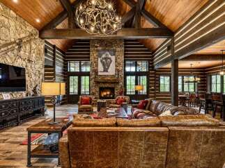 Experience rustic luxury in this stunning log cabin living room, featuring a grand stone fireplace as the centerpiece and a magnificent antler chandelier.