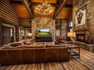 Experience rustic luxury in this stunning log cabin living room, featuring a grand stone fireplace and a magnificent antler chandelier.