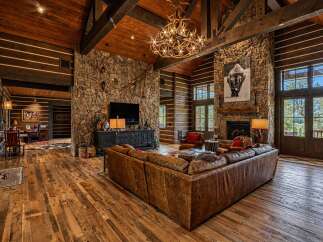 Experience rustic luxury in this stunning log cabin living room, featuring a grand stone fireplace and a magnificent antler chandelier.