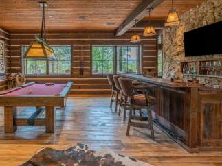 Experience ultimate relaxation and entertainment in this stunning log cabin game room, featuring a professional pool table and a fully equipped bar area.