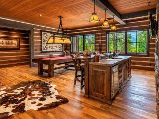 Experience rustic luxury in this stunning game room, featuring a classic billiard table and a fully equipped bar area with a granite countertop.