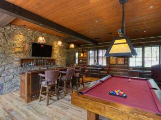 Experience ultimate relaxation and entertainment in this rustic lodge-style game room, featuring a full-service bar with stone accents and comfortable seating.