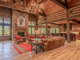 Experience rustic luxury in this stunning log cabin living room, featuring a grand stone fireplace and a magnificent antler chandelier.