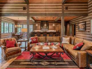 Experience rustic luxury in this stunning log cabin living room, featuring a spacious sectional sofa and a cozy armchair perfect for relaxation.
