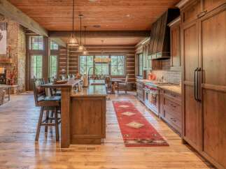 Experience rustic luxury in this stunning log cabin kitchen, featuring a spacious island with bar seating and a professional-grade range under a custom metal hood.
