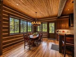 Experience rustic luxury in this stunning log cabin dining room, featuring a grand wooden table surrounded by chairs with vibrant, patterned upholstery.