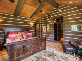 Experience rustic luxury in this stunning log cabin bedroom, featuring a grand wooden bed adorned with vibrant pillows and a cozy striped throw.