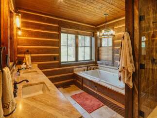Experience rustic luxury in this stunning log cabin bathroom, featuring a deep soaking tub and a spacious dual vanity with travertine countertops.
