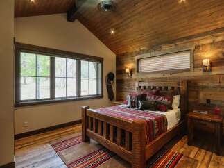 Experience rustic charm in this cozy bedroom featuring a robust wooden bed adorned with a patterned blanket and accent pillows.