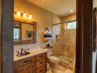 Experience rustic charm in this beautifully appointed bathroom, featuring a custom wooden vanity with a copper sink and a spacious walk-in shower with stone tile accents.