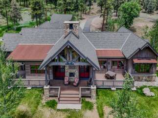 Experience rustic luxury in this stunning mountain lodge, featuring a grand stone fireplace and expansive covered porch perfect for enjoying the serene surroundings.