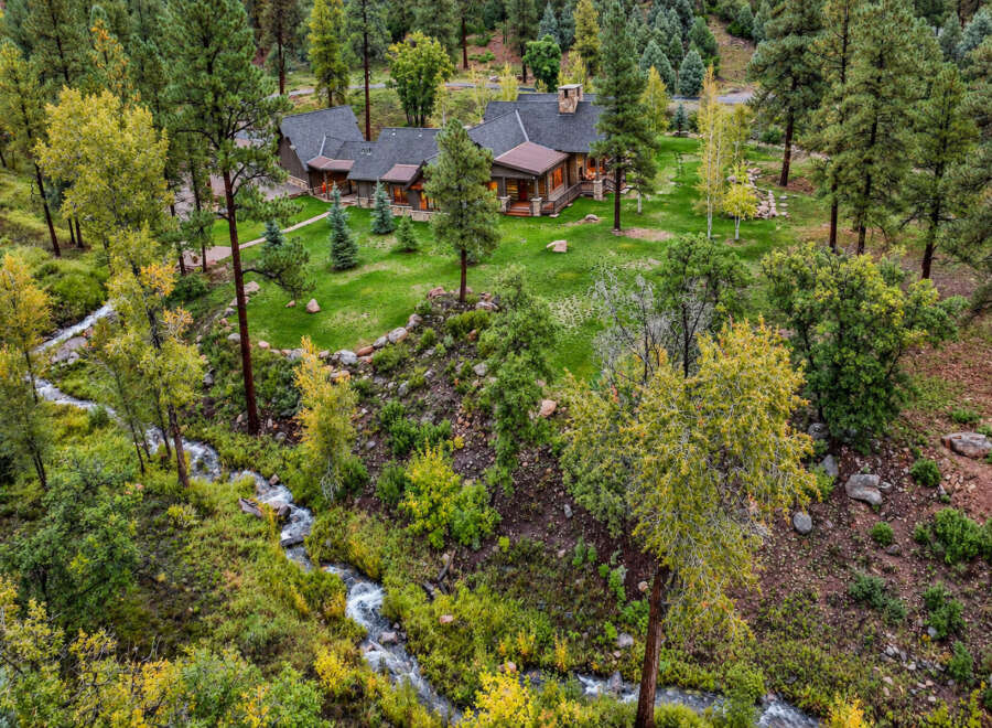 Nestled amidst a lush forest, this stunning property features a beautiful home with a charming porch and a stone chimney.