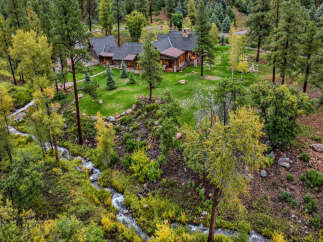 Nestled amidst a lush forest, this stunning property features a beautiful home with a charming porch and a stone chimney.