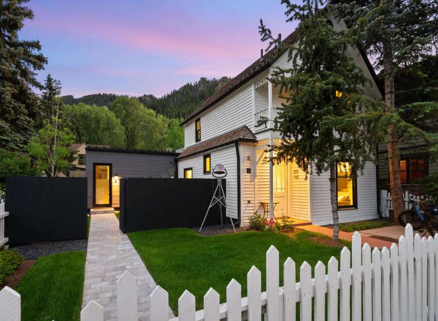 Charming white clapboard home with a white picket fence and lush green lawn, set against a backdrop of rolling hills and a vibrant twilight sky.