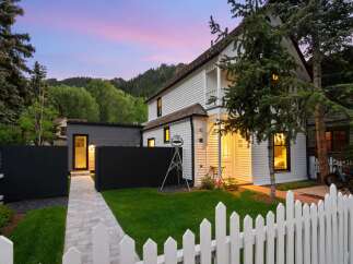 Charming white clapboard home with a white picket fence and lush green lawn, set against a backdrop of rolling hills and a vibrant twilight sky.