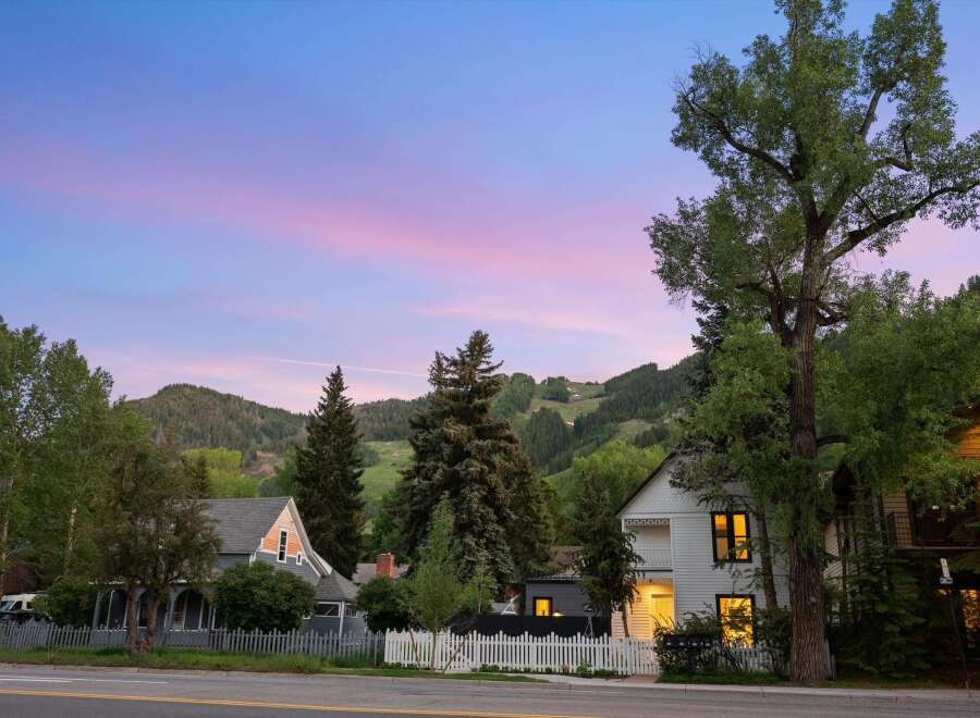 Charming homes nestled against a backdrop of lush green mountains under a vibrant twilight sky.