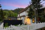Charming white clapboard home with a white picket fence, nestled against a backdrop of lush green trees and majestic mountains.