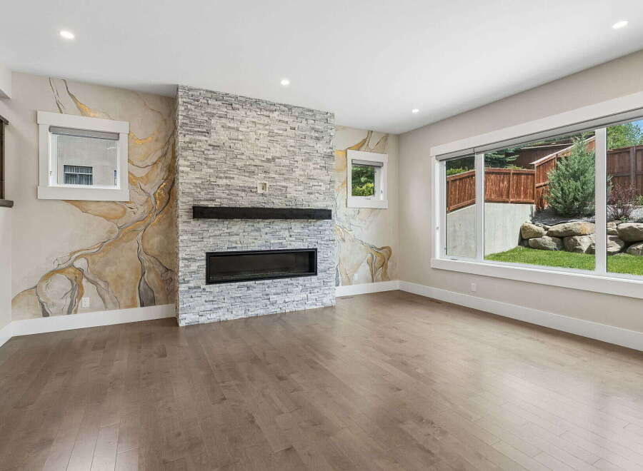 Experience modern living in this stunning living room featuring a striking stone fireplace and a unique marble-inspired accent wall.