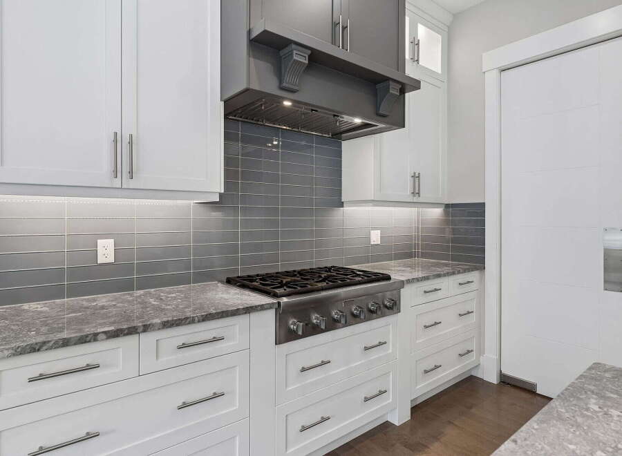 Experience culinary excellence in this modern kitchen, featuring a professional-grade gas range and a sleek grey subway tile backsplash.