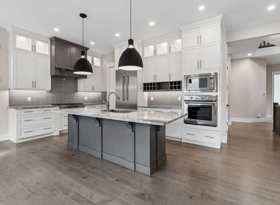 Experience luxury in this stunning modern kitchen, featuring sleek white cabinetry, a sophisticated grey island with a marble countertop, and high-end stainless steel appliances.