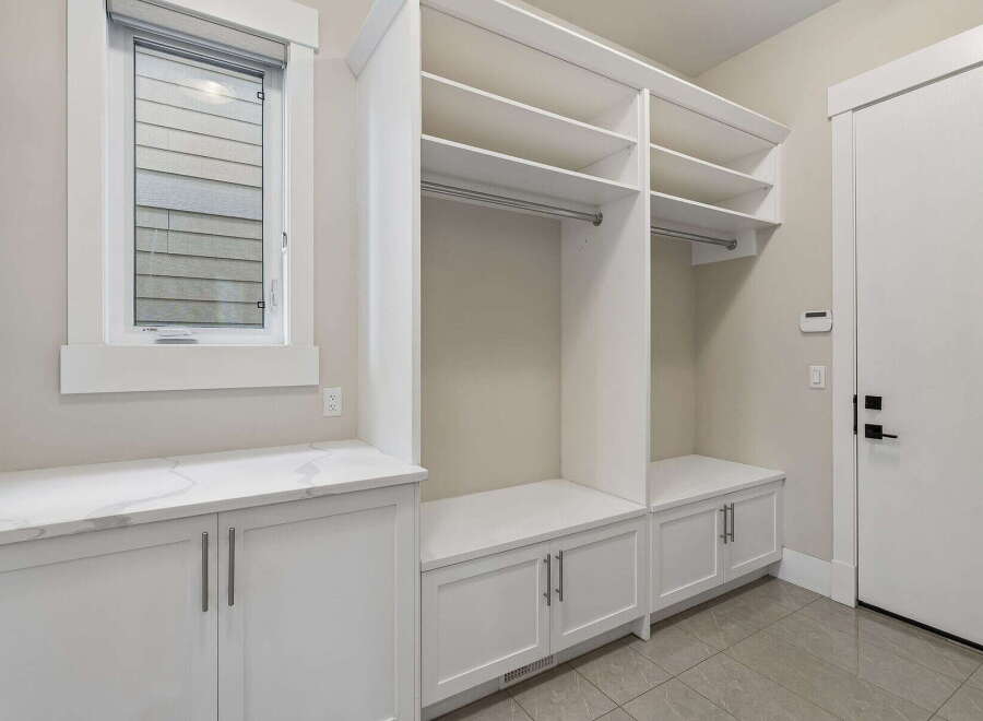 This spacious mudroom features ample storage with built-in white cabinets and shelving, perfect for organizing outerwear and accessories.