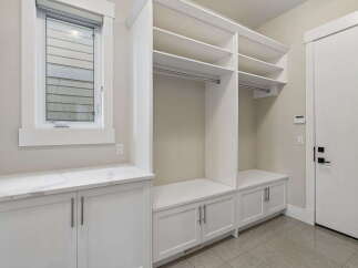 This spacious mudroom features ample storage with built-in white cabinets and shelving, perfect for organizing outerwear and accessories.