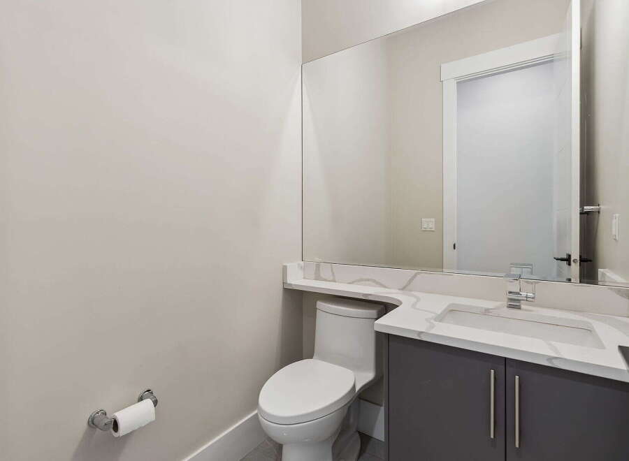 This modern powder room features a sleek vanity with a quartz countertop and a minimalist sink, complemented by a large mirror that enhances the sense of space.