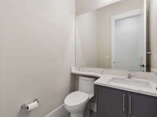 This modern powder room features a sleek vanity with a quartz countertop and a minimalist sink, complemented by a large mirror that enhances the sense of space.