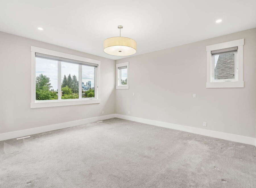 This spacious bedroom features a large picture window offering scenic views of trees and city skyline.
