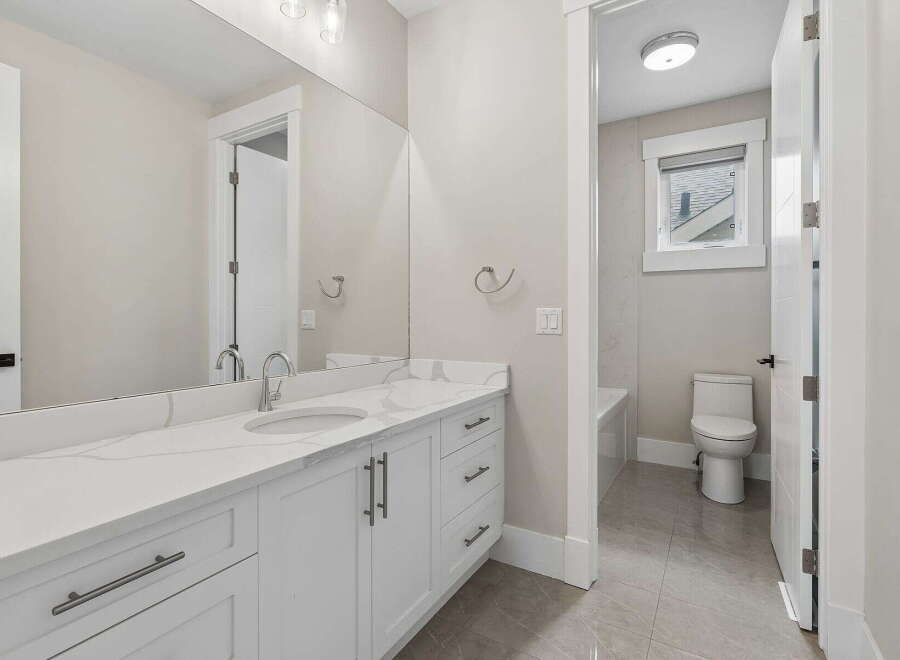 This modern bathroom features a sleek white vanity with a quartz countertop and undermount sink, complemented by a large vanity mirror.