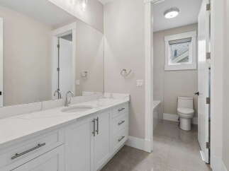 This modern bathroom features a sleek white vanity with a quartz countertop and undermount sink, complemented by a large vanity mirror.