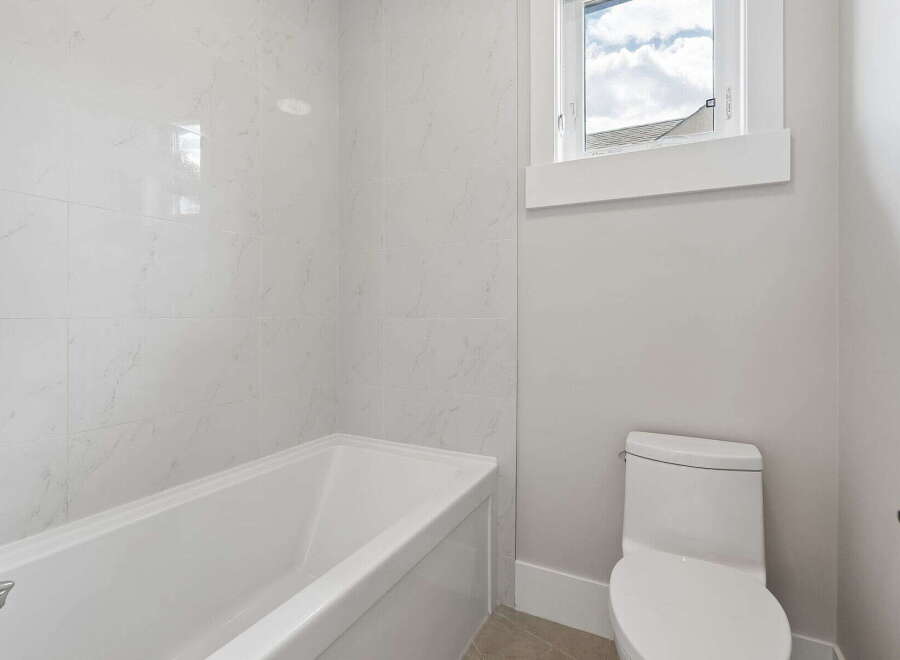 This modern bathroom features a sleek white bathtub with marble-patterned tile walls, creating a spa-like ambiance.