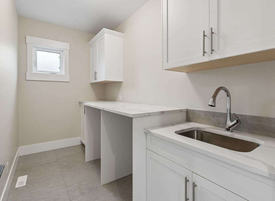 Discover this modern laundry room featuring a sleek white countertop with a marble-like finish, complemented by a deep stainless steel sink and a high-arc faucet.
