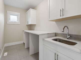 Discover this modern laundry room featuring a sleek white countertop with a marble-like finish, complemented by a deep stainless steel sink and a high-arc faucet.