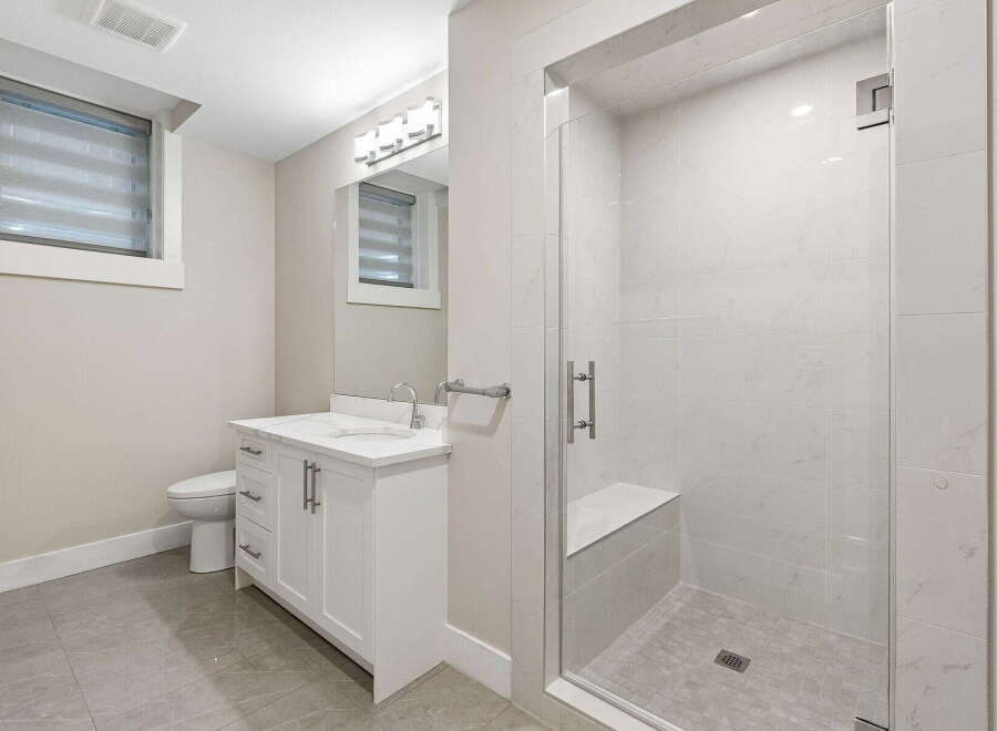This modern bathroom features a sleek white vanity with a double sink, complemented by a spacious walk-in shower with a built-in bench and elegant marble-look tiles.