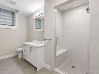 This modern bathroom features a sleek white vanity with a double sink, complemented by a spacious walk-in shower with a built-in bench and elegant marble-look tiles.