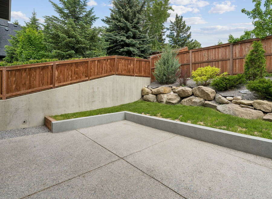 This backyard features a modern concrete patio, perfect for outdoor entertaining, bordered by a raised garden bed with lush green grass.