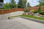This backyard features a modern concrete patio, perfect for outdoor entertaining, bordered by a raised garden bed with lush green grass.