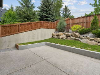 This backyard features a modern concrete patio, perfect for outdoor entertaining, bordered by a raised garden bed with lush green grass.