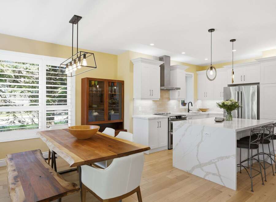 Experience modern living in this stunning kitchen and dining area, featuring a sleek white island with quartz countertops and a live-edge dining table.