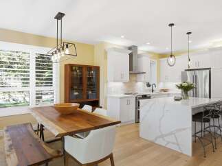Experience modern living in this stunning kitchen and dining area, featuring a sleek white island with quartz countertops and a live-edge dining table.